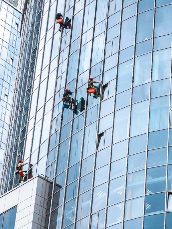 Operarios certificados realizando limpieza de fachadas vidriadas en altura con equipo de seguridad.